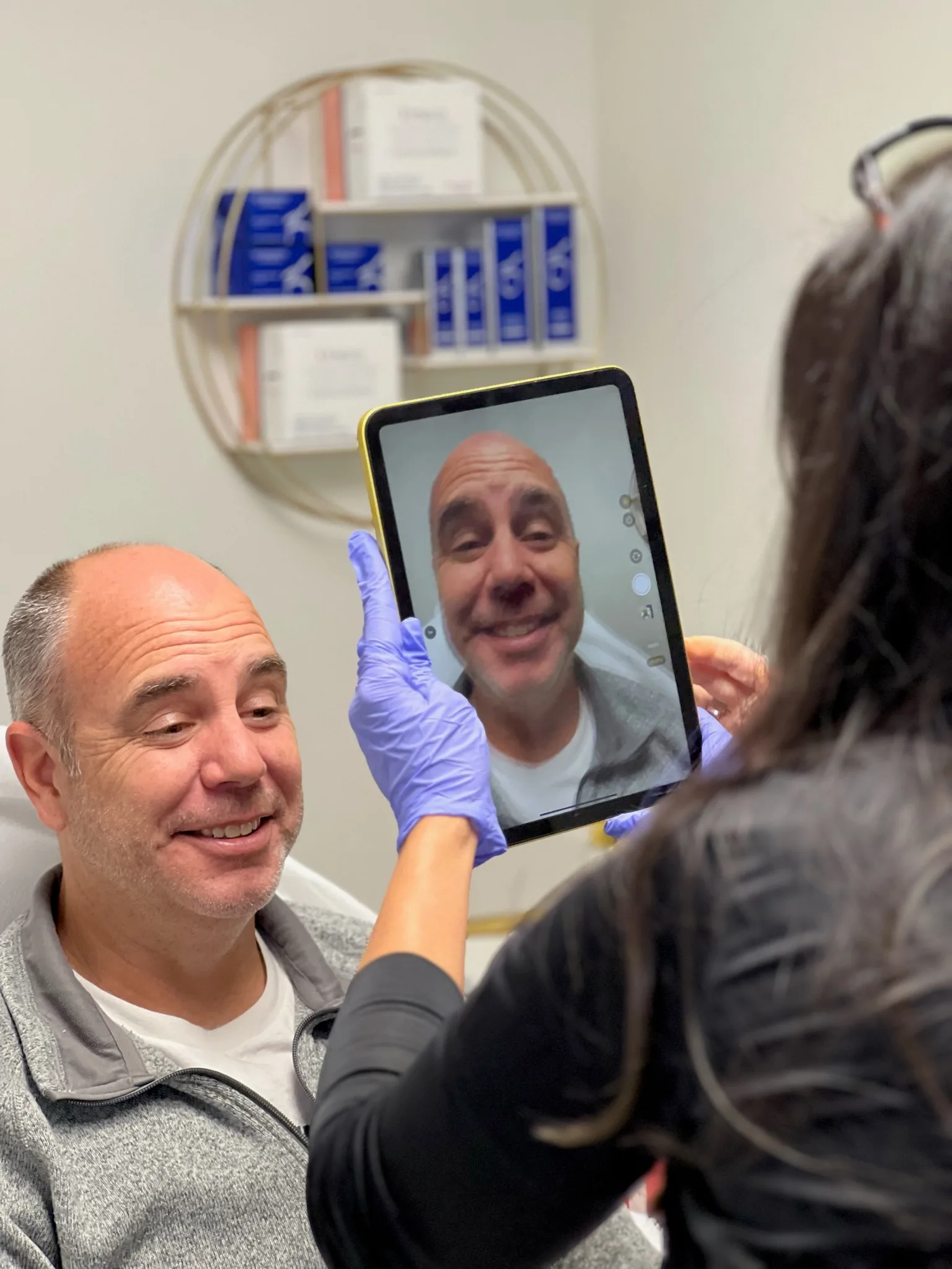 A smiling live model holds a mirror during a supervised Academy practice session